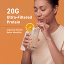 A woman in a beige top drinks from a glass of iced beverage with an orange slice garnish, set against an orange background with text reading '20G Ultra-Filtered Protein' and 'Improved Taste & Better Mixability'.