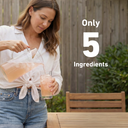 A woman in a white shirt and blue jeans pours a pink drink from a clear glass pitcher into a glass tumbler outdoors. A wooden fence, bench, and greenery are in the background, with large white text reading 'Only 5 Ingredients'.